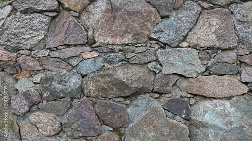 Beautiful rough stonework made of solid granite boulders and small pebbles, a fragment of a wall or fence made of natural rock, the texture of the stone material in the structure of the exterior