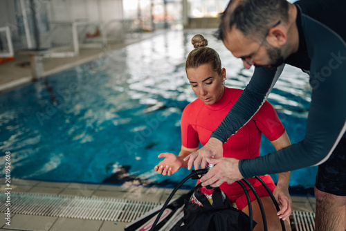 Konstfotografi Scuba diving instructor teaching woman about gear setup near swimming pool, prep