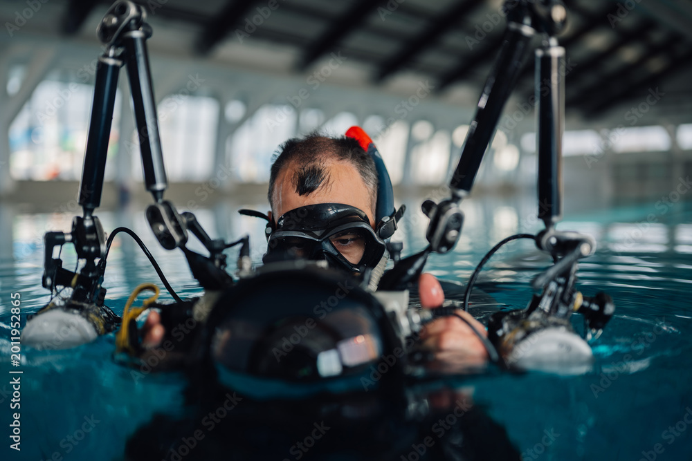 Fototapeta premium Scuba diver holding underwater camera equipment in a swimming pool, preparing for practice and training
