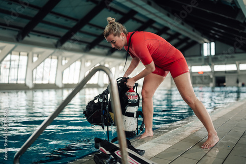 Foto Woman in a red wetsuit preparing scuba gear for a dive in a swimming pool, pract