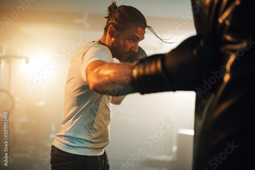 Photos Man training boxing in a gym, hitting a punching bag