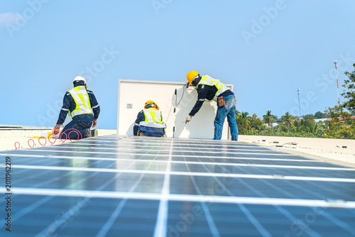 Foto Two solar technicians working together to align and bolt down photovoltaic modules on a commercial roof during a sunny day