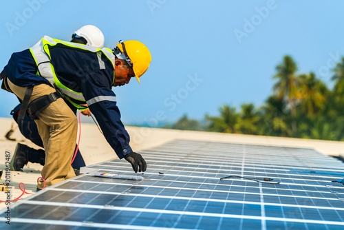 Foto A professional technician in safety gear standing on a rooftop, preparing electrical wiring for a solar panel installation under a clear blue sky
