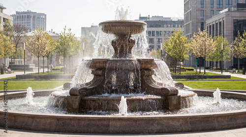 Urban round cascading stone fountain in a public garden surrounded by houses and office buildings