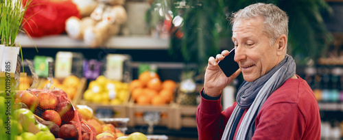 A person is talking on a mobile phone while standing near a display of fruits at a grocery store. The store has many colorful fruits on display.