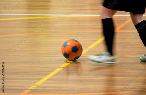 Indoor soccer player dribbling ball on wooden court, futsal, with motion blur