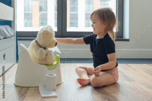 Foto Little child and teddy bear sitting on plastic baby potties indoors