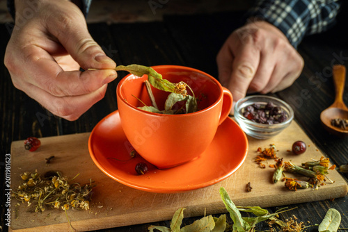 Vászonkép A person adds dried leaves and flowers into an orange cup to make herbal tea