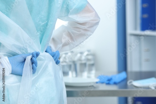 Фотография Medical worker tying disposable isolation gown indoors, closeup