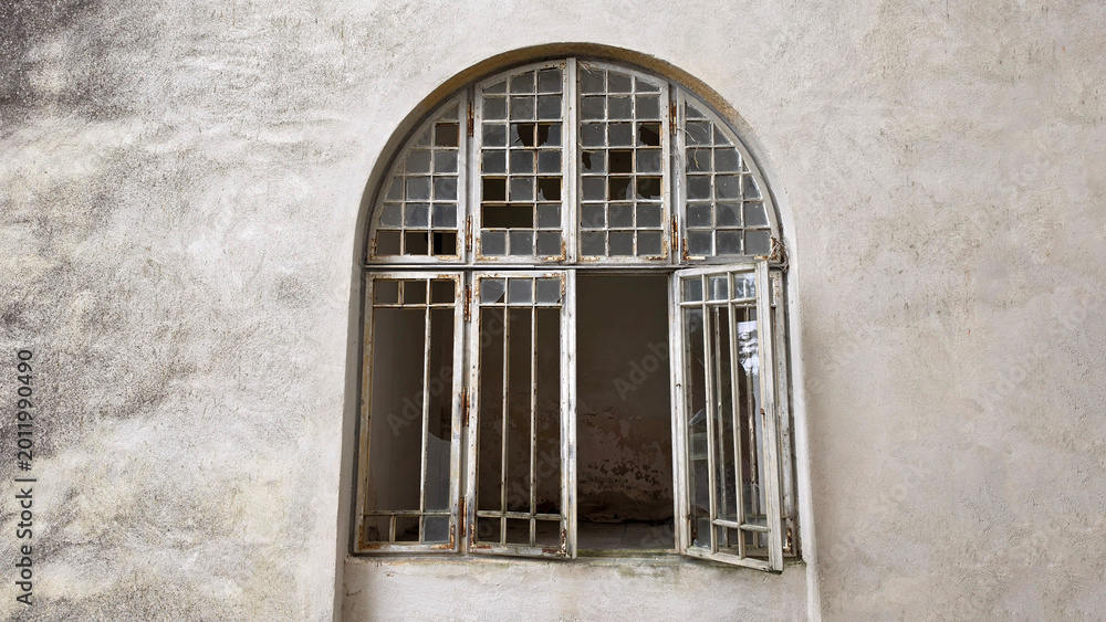 Obraz premium Arched vintage window with broken glass panes in a weathered stone wall