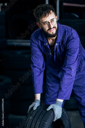 Mechanic in blue overalls and gloves working with car tire, providing professional vehicle service and maintenance