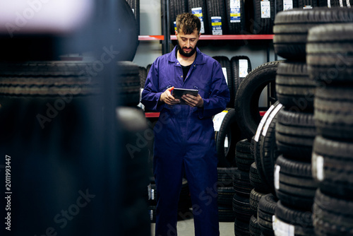 Canvas Print Technician in blue overalls managing tire stock and sales in a warehouse, utiliz