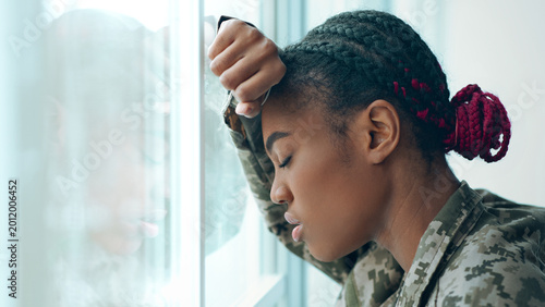 Fotografie A woman in a military uniform stands next to a window with her hand on her forehead