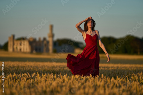 Woman rye field red dress. Happy woman in a long red dress in a beautiful cornfield. Old caste ruins in the background