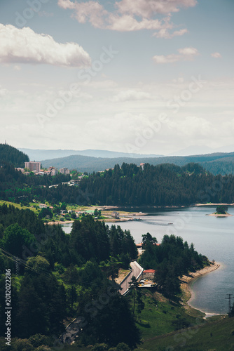 Scenic lake landscape with forested hills, small village and winding road, aerial view of peaceful countryside with water and mountains under soft daylight