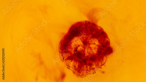 Dark red ink sphere spreading through warm yellow liquid in abstract macro composition