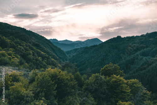 panoramic mountain landscape with green forested hills under dramatic cloudy sky at sunset
