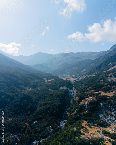 Aerial view of a dramatic mountain valley with a river flowing through rugged terrain. Misty mountain peaks and layered hills create a serene natural landscape, perfect for travel, wilderness, and env
