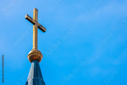Golden cross atop a church steeple against a clear blue sky, showcasing architectural details and a prominent religious symbol in a serene outdoor setting