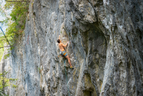 Fotografija Male athlete climbs a challenging overhanging section on a steep limestone wall