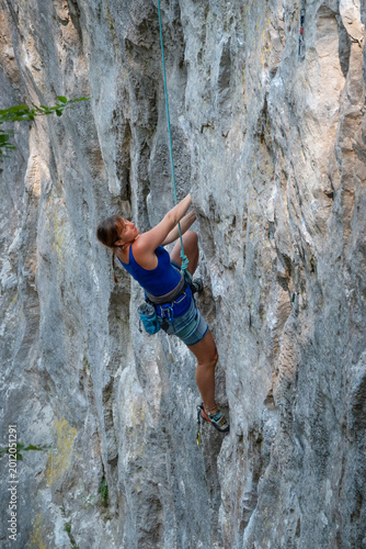 Принти на полотні Young woman climbs a steep limestone route while secured on rope and equipped with climbing gear
