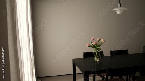 Modern, minimalist dining area and kitchen in a contemporary apartment. Sleek dark wooden dining table set with a glass vase of pink tulips, surrounded by designer chairs