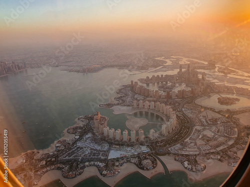 Golden hour aerial view of The Pearl-Qatar and Doha coastline photographed from an airplane window during descent over Qatar.