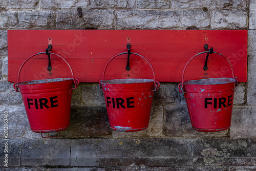 Three old red fire buckets hanging on a stone wall