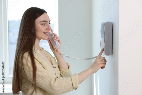 Bild auf Leinwand Young woman answering intercom call at home