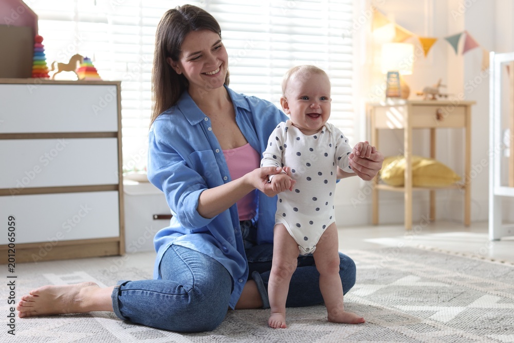 Obraz premium First steps. Mother supporting daughter while she learning to walk at home