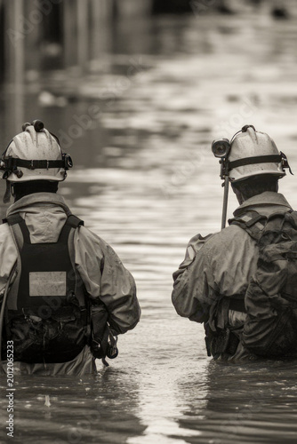 Two firefighters walking through a flooded street vertical frame