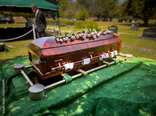 Photography A casket with pallbearer gloves covered in roses at a gravesite