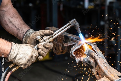 Metalworker using an oxyacetylene cutting torch on rusty steel causing bright sparks
