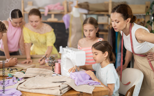 Φωτογραφία Woman teacher oversees teen girl childs work on sewing machine, practical classes at school of young designers and tailors