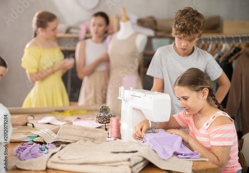 Tablou pe pânză Girl sews on a sewing machine. A boy watches and learns