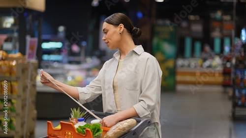 Woman checking long shopping list in supermarket aisle