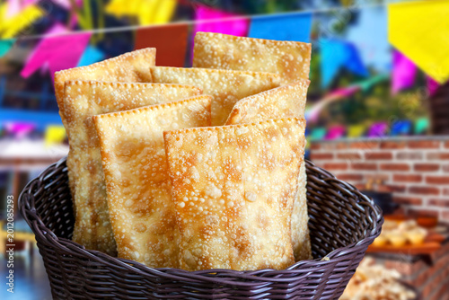 Crispy golden Brazilian fried pastels served at a traditional Festa Junina celebration, decorated with colorful flags and a sunny outdoor background.