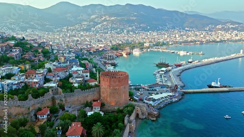 Wide aerial view of Red Tower in Alanya. Historic stone tower overlooks the harbour, coastal city and Mediterranean Sea.