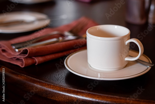 Tableau sur toile White Coffee Cup on Wooden Table with Napkin and Cutlery – Cozy Restaurant Setti