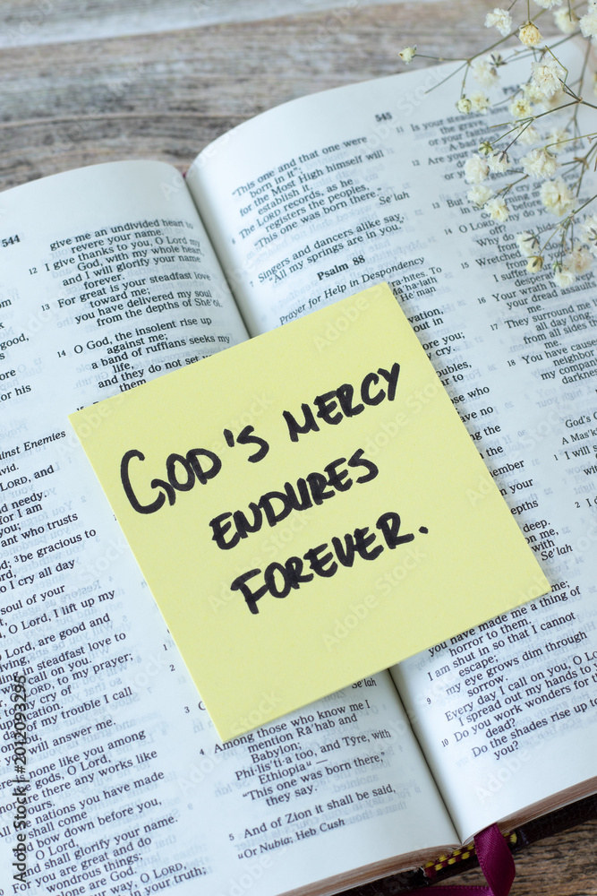 Obraz premium God's mercy endures forever, inspirational quote with holy bible on wooden background. Jesus Christ's grace, compassion, and forgiveness, biblical concept.