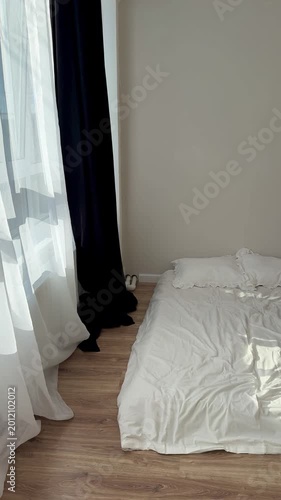 Sunlit mattress with white sheet on wooden floor beside sheer curtains, morning light casting soft shadows across rumpled bedding