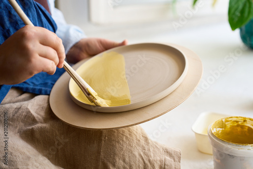 Creative ceramic surface design with a broad brush and yellow glaze on a flat plate.