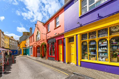 A narrow street of vibrant, multicolored storefronts in the historic center of Kinsale, a fishing port town in County Cork, Ireland.