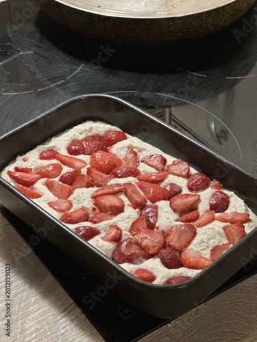 Healthy homemade cottage cheese casserole topped with fresh strawberries in a black baking dish on a modern kitchen countertop with a frying pan in the background