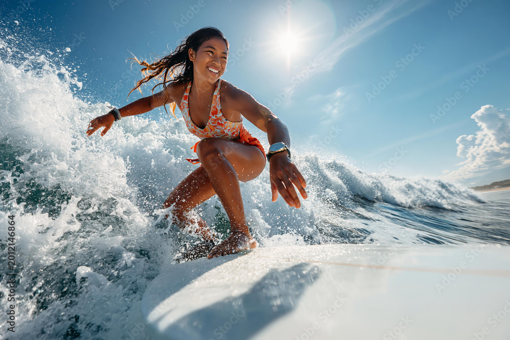 Fototapeta premium Young woman happily surfing a wave under the bright sun