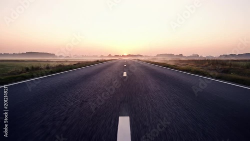 POV driving on long straight road towards sunrise in morning mist