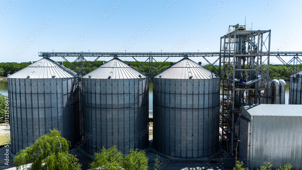 Fototapeta premium Large industrial grain silos with processing tower at a riverside facility