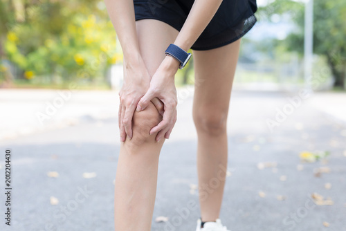 Female runner holding her knee experiencing severe pain and physical discomfort after an outdoor injury stopping on road touching hurting leg joint showing suffering during an exercise routine