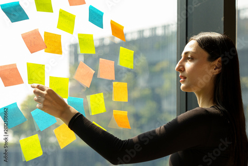 A focused young professional woman planning and organizing ideas using vibrant sticky notes on a glass window. The images capture a creative workflow, project management, and strategy development in a
