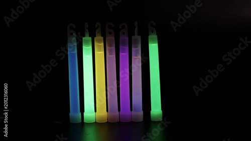 Schilderij op canvas Row of Seven Colorful Glowing Light Sticks Against a Dark Background